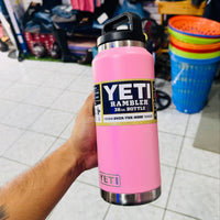 Pink YETI Rambler bottle held by a person in an indoor setting with various items in the background.