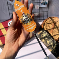 Hand holding a Harry Potter-themed pen with an orange handle against a casual indoor background