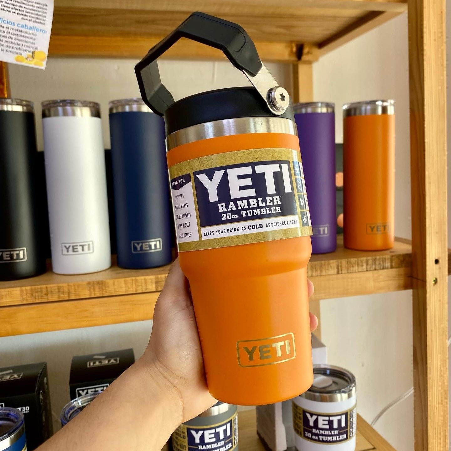 Orange YETI Rambler tumbler held in front of a shelf with various YETI products.