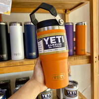 Orange YETI Rambler tumbler held in front of a shelf with various YETI products.
