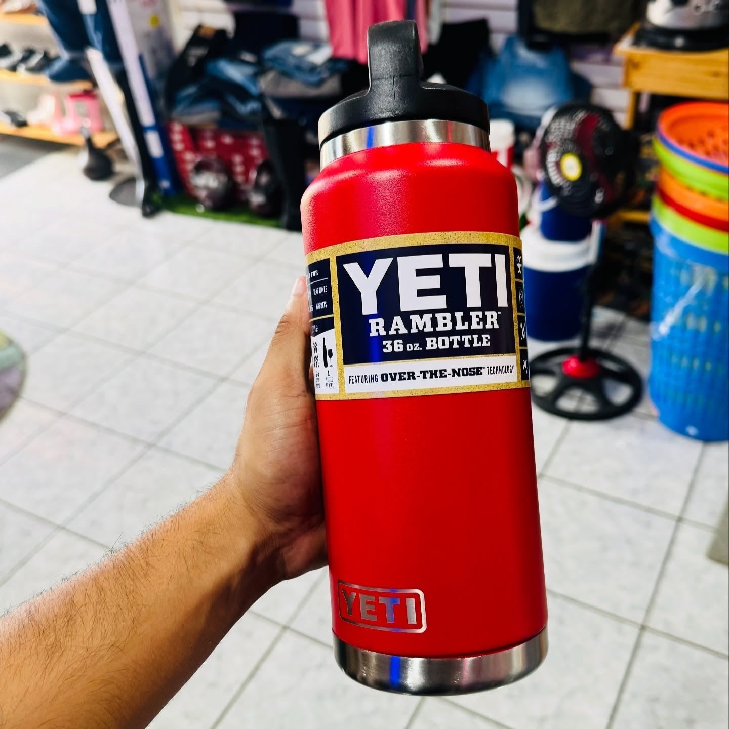 Red YETI Rambler bottle held by a person in an indoor setting with various items in the background.