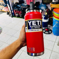 Red YETI Rambler bottle held by a person in an indoor setting with various items in the background.