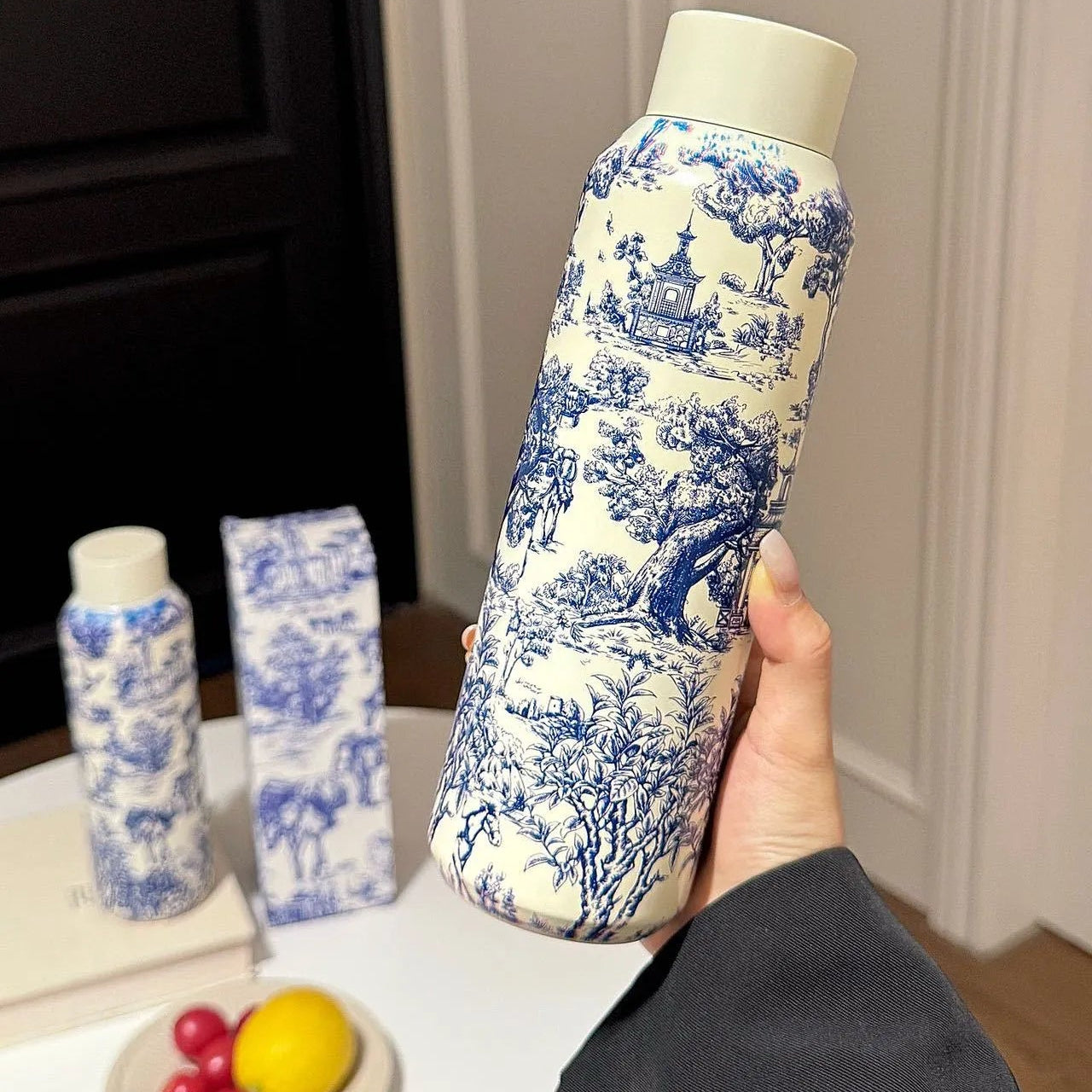 Dior Bottle with blue and white floral pattern held by a hand on a neutral background