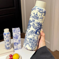Dior Bottle with blue and white floral pattern held by a hand on a neutral background