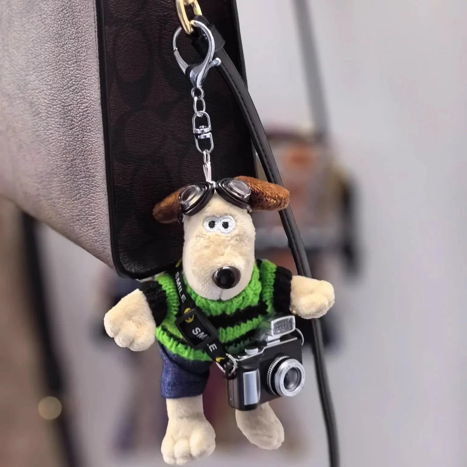 Gromit dog-shaped keychain with a camera attached to a handbag.