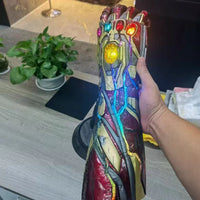 Colorful iron man hand held by another hand on a desk with plants in the background