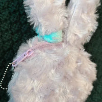 Close-up of a fluffy pink toy with a pink zipper and chain detail on a textured green background.