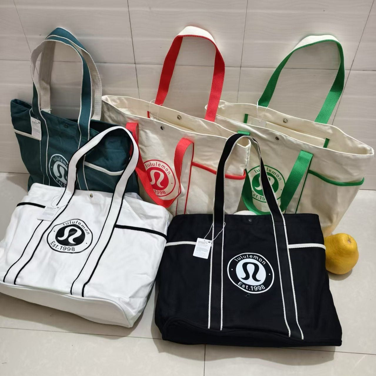 Five tote bags with a visible brand logo on a tiled floor.
