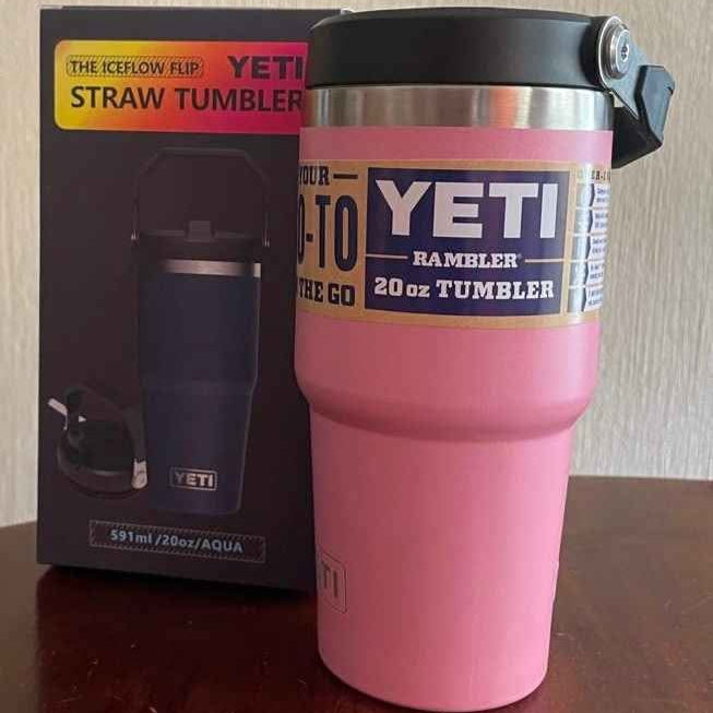 Pink YETI tumbler with black lid next to its packaging on a wooden surface.