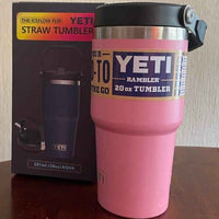 Pink YETI tumbler with black lid next to its packaging on a wooden surface.