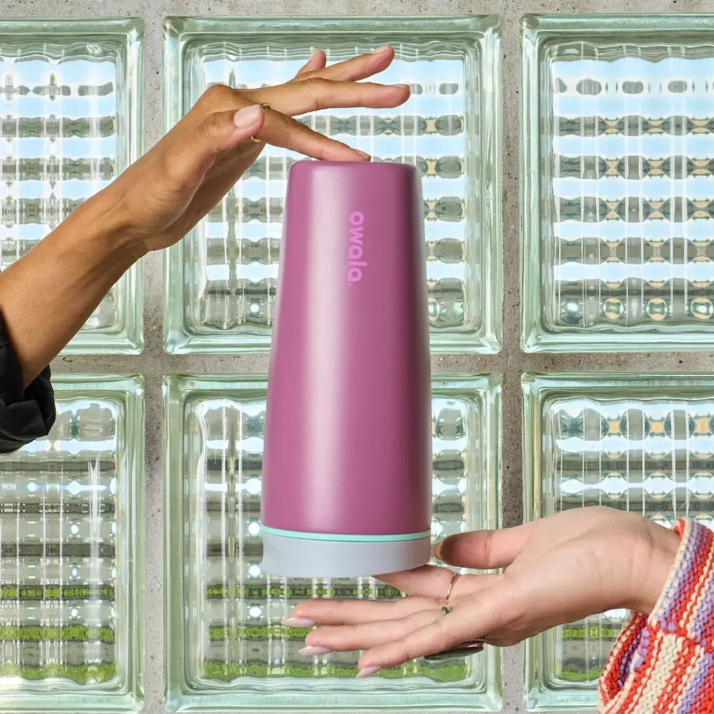 Pink tumbler with a hand reaching for it against a glass block wall background