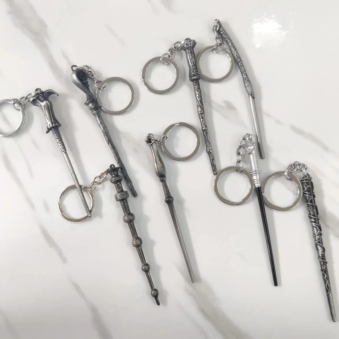 Silver keychains shaped like wands on a white background
