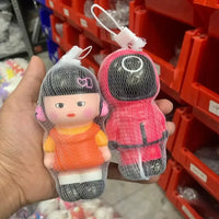 Two small dolls in clear bags held in front of red storage shelves.